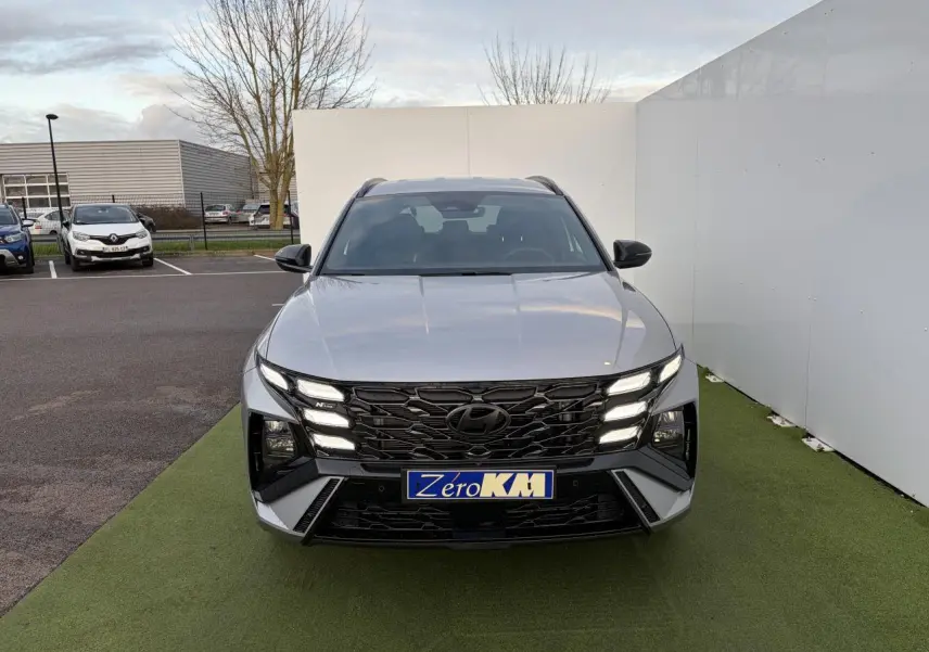 Vue avant d'un Hyundai Tucson 2025 gris argent métallisé avec calandre noire N Line et feux LED allumés.