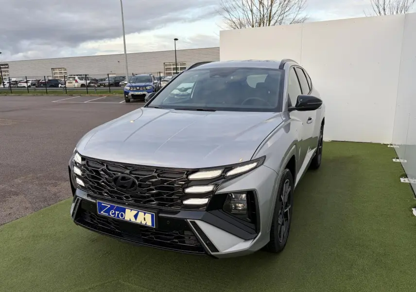 Vue 3/4 avant d'un Hyundai Tucson 2025 gris argent métallisé avec calandre noire et jantes alliage sombres.