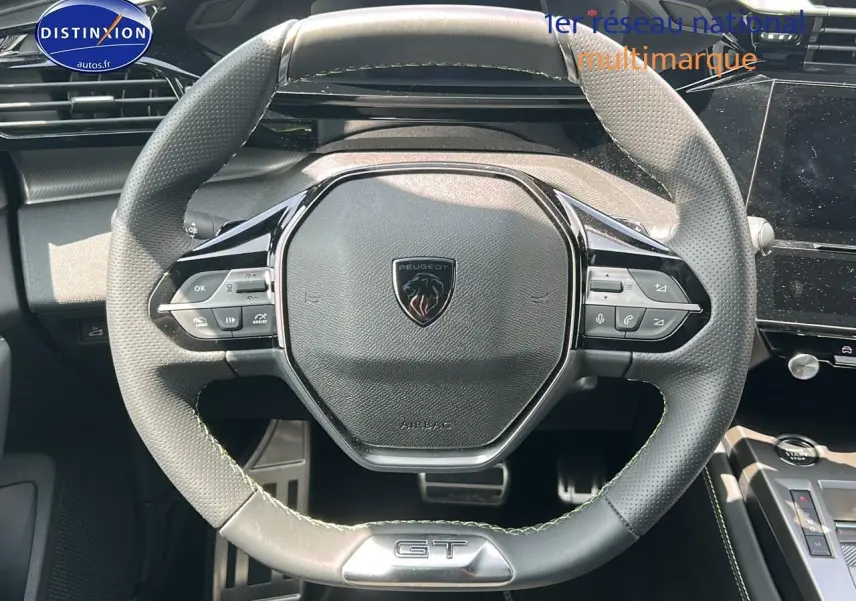 Vue rapprochée du volant cuir noir perforé avec logo Peugeot et badge GT du Peugeot 408 Hybrid 145 GT 2024.