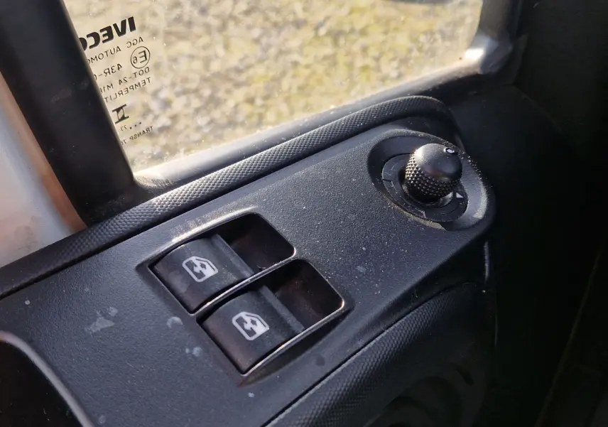 Gros plan sur les commandes de lève-vitres et réglage des rétroviseurs côté gauche d’un Iveco Daily Fourgon blanc.