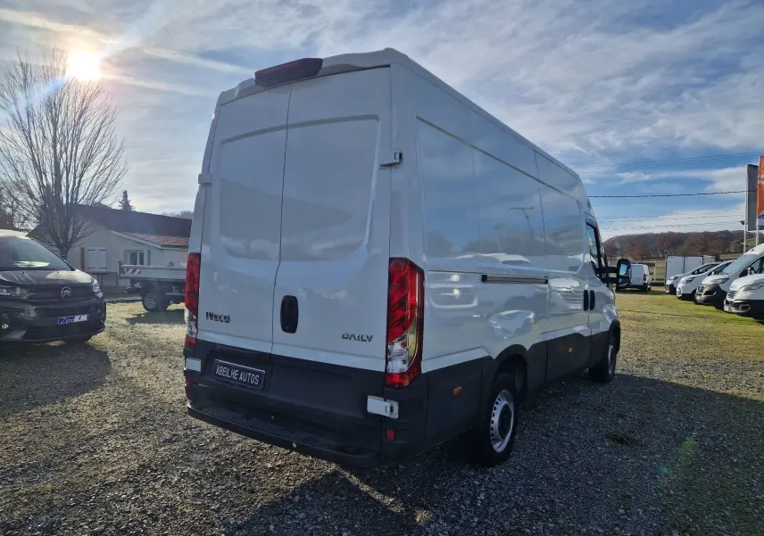 Vue 3/4 arrière droite d'un utilitaire Iveco Daily blanc 2023 avec portes arrière fermées sur un parking extérieur.