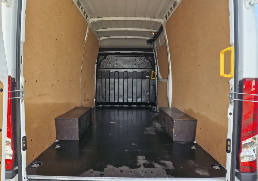 Vue intérieure arrière du fourgon Iveco Daily blanc 2023, montrant l'espace de chargement avec parois en bois et sol noir antidérapant.