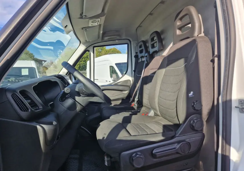 Vue intérieure côté conducteur du fourgon blanc Iveco Daily 35S16 avec sièges noirs et tableau de bord simple.
