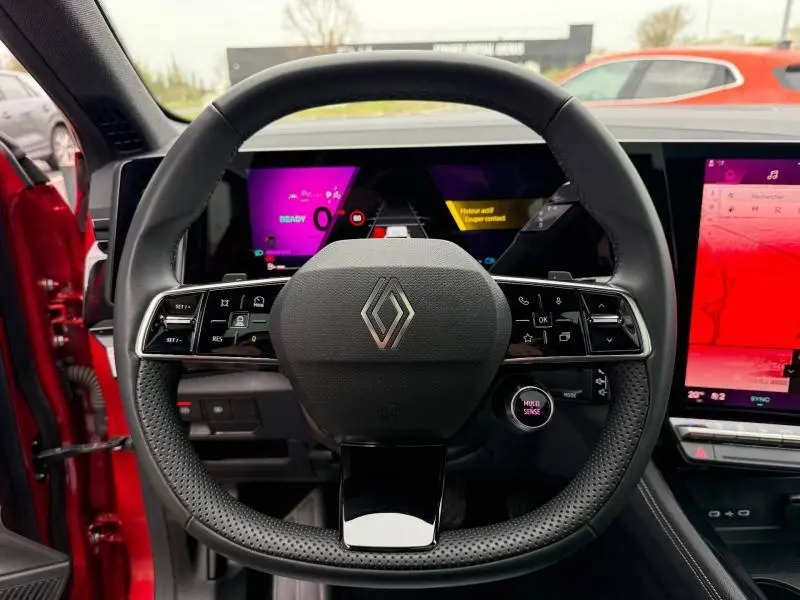 Vue centrée sur le volant perforé du Renault Austral Rouge Flamme 2025 avec tableau de bord numérique et écran tactile.