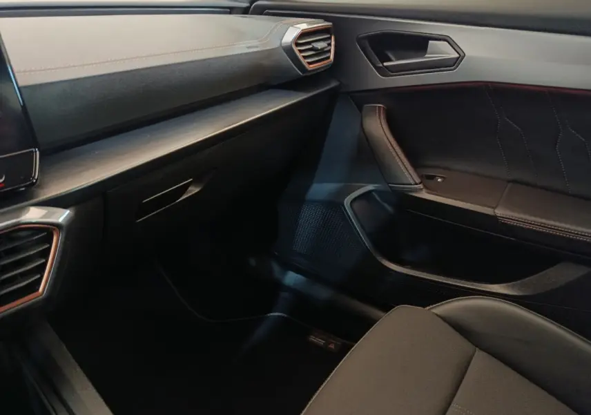 Vue intérieure côté passager du tableau de bord et de la porte avec finitions noires et surpiqûres contrastantes.