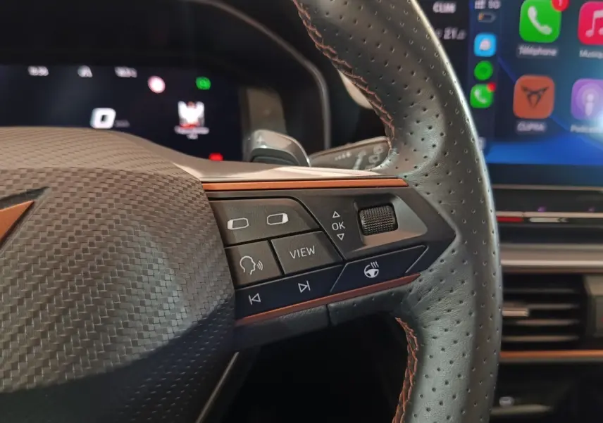 Gros plan sur le volant noir perforé du CUPRA Formentor 2024 avec commandes multifonctions et écran tactile en arrière-plan.