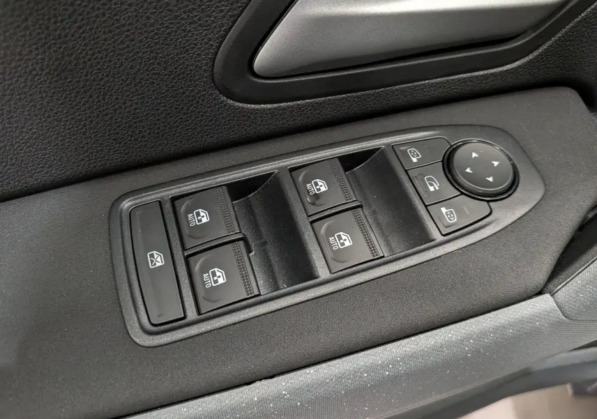 Gros plan sur les commandes des vitres électriques et rétroviseurs du côté gauche intérieur du Dacia Duster blanc Glacier.