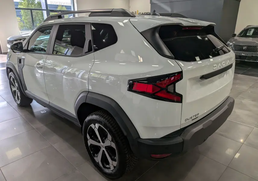 Vue 3/4 arrière droite du Dacia Duster Hybrid-G blanc Glacier, avec jantes biton et éléments noirs contrastants.