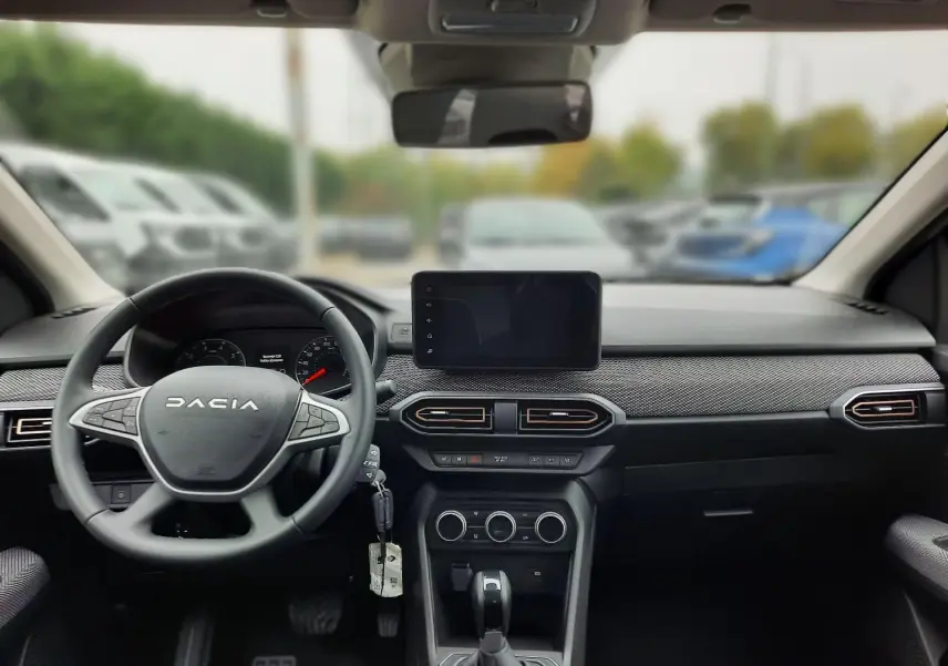 Vue intérieure avant du tableau de bord noir de la Dacia Sandero Stepway 2025 avec volant multifonctions et écran tactile central.