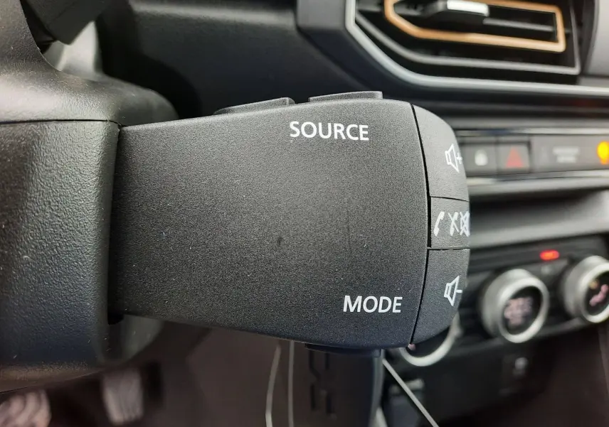 Gros plan sur la commande audio au volant du Dacia Sandero Stepway 2025 noir nacré, avec tableau de bord flou en arrière-plan.