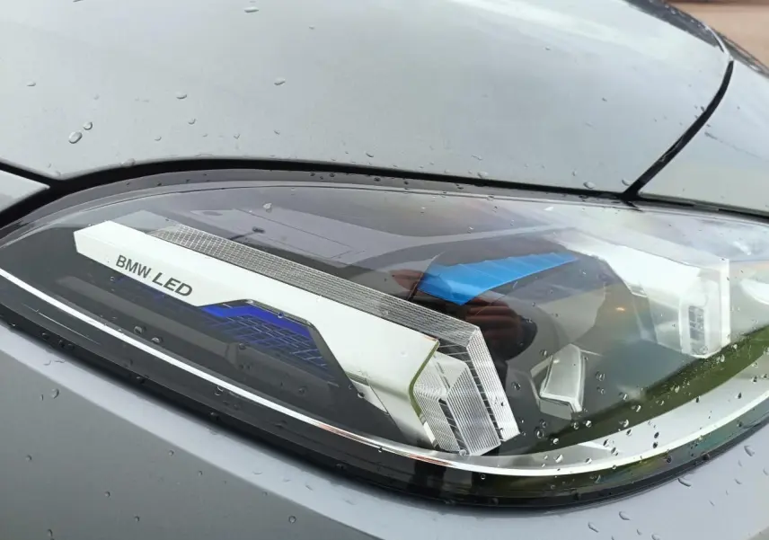 Gros plan sur le phare avant droit LED d'une BMW Série 1 gris Skyscraper avec toit noir, gouttes de pluie visibles.