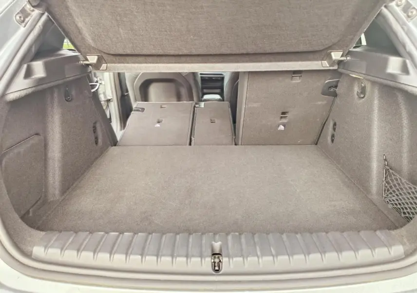 Coffre ouvert de BMW Série 1 gris, banquette arrière rabattue partiellement côté droit, vue depuis l'arrière.