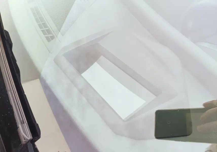 Vue intérieure du tableau de bord de la BMW Série 1 2025 gris Skyscraper avec écran et toit noir visible en reflet.