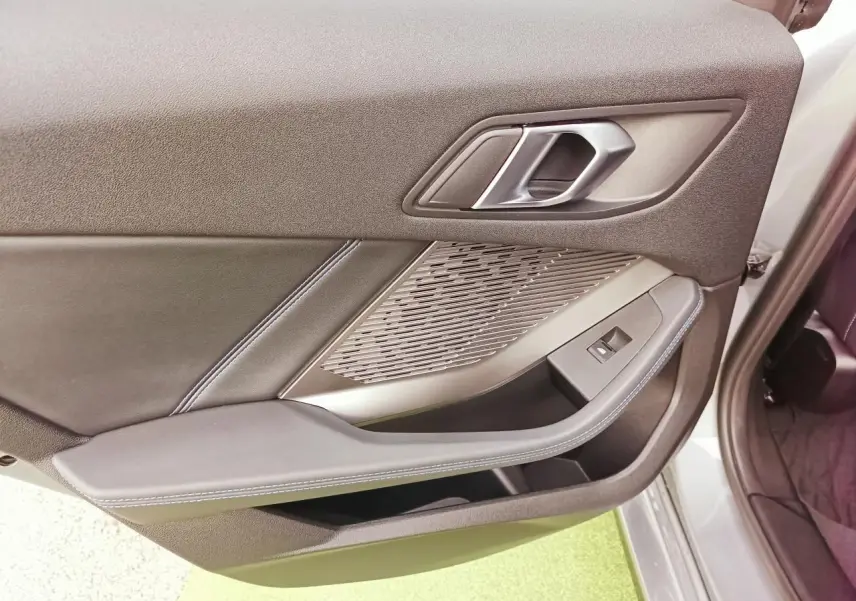 Vue rapprochée de la porte avant droite de la BMW Série 1 2025, habillage noir avec surpiqûres bleues et insert aluminium.