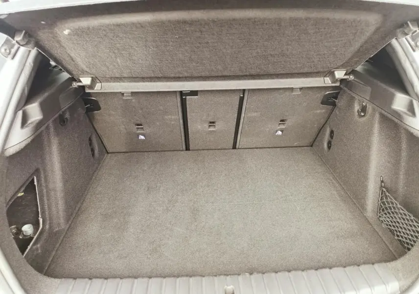 Coffre ouvert de BMW Série 1 F70 gris Skyscraper, vue intérieure montrant la banquette arrière rabattable et filet de rangement côté droit.