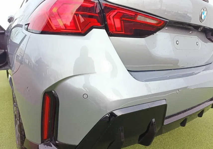 Vue 3/4 arrière droite d'une BMW Série 1 gris Skyscraper avec feux LED distinctifs et diffuseur noir brillant.