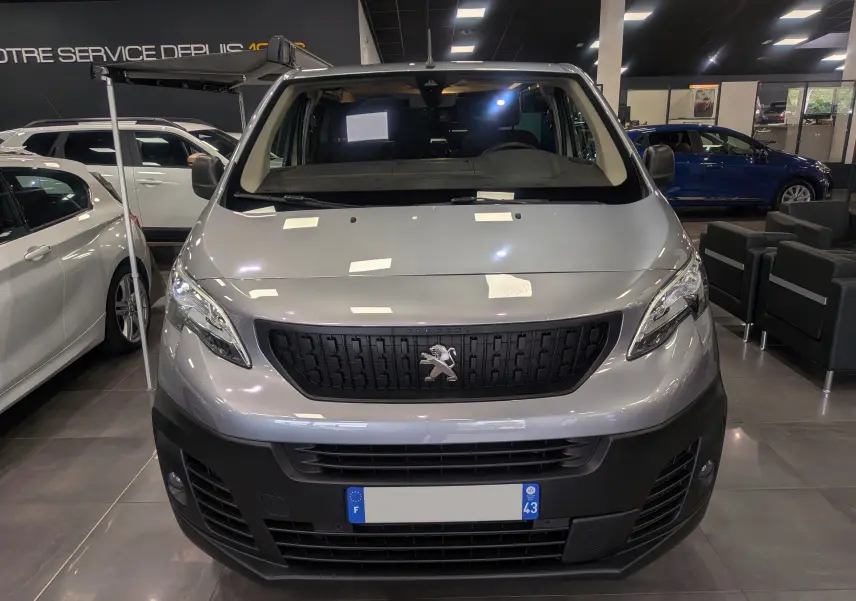Vue de face d’un Peugeot Expert Fourgon gris acier aménagé, avec store latéral déployé en intérieur showroom.