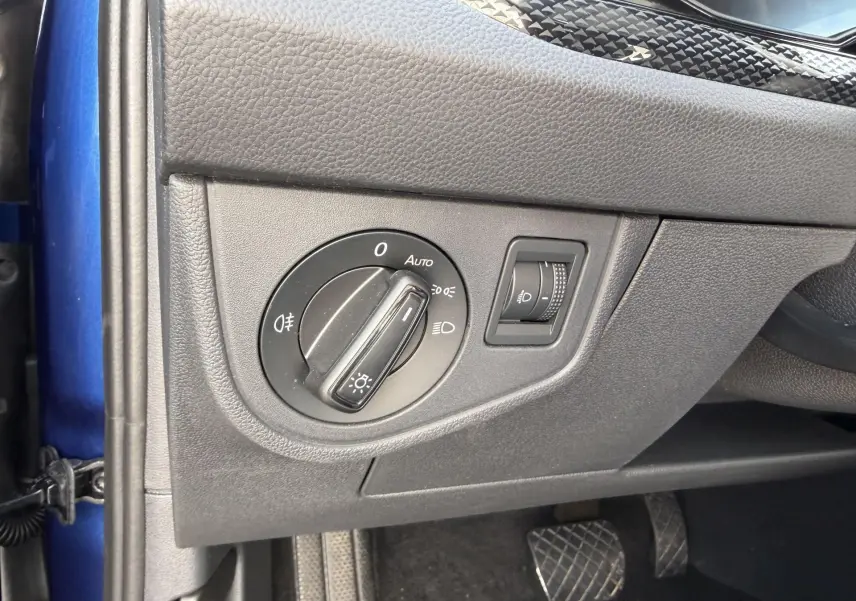 Vue intérieure côté gauche du tableau de bord bleu du Volkswagen Taigo 2025, avec commande des phares et réglage de l'éclairage.