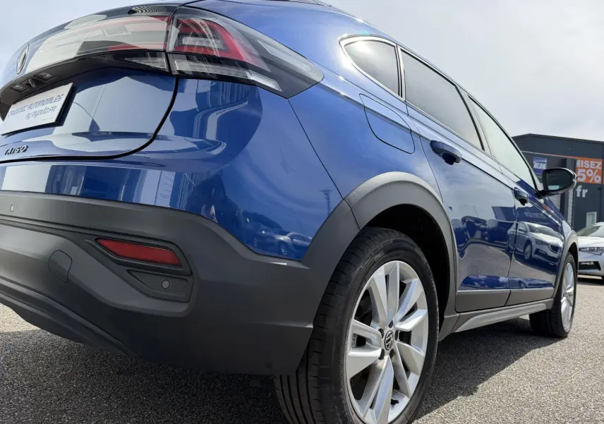 Vue 3/4 arrière droite du Volkswagen Taigo bleu métallisé avec jantes alliage et protections noires sur les passages de roues.