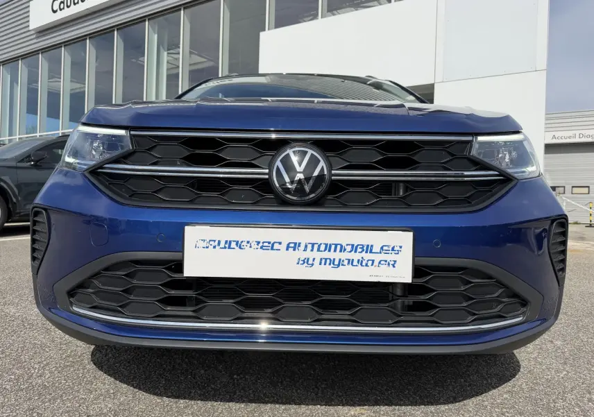 Vue frontale rapprochée d’un Volkswagen Taigo bleu métallisé avec calandre noire à motifs hexagonaux.