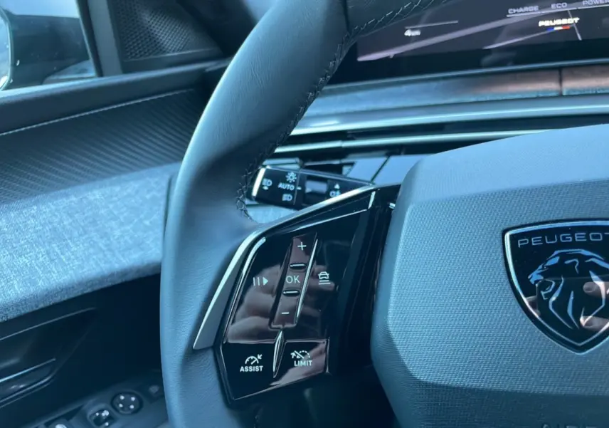 Gros plan sur le volant cuir du Peugeot 5008 Hybrid 145 Allure Plus gris titane avec commandes multifonctions et logo lion.