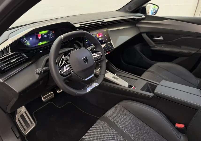 Intérieur avant droit de la Peugeot 308 Hybrid 136 e-DCS6 GT 2024 avec volant cuir et écran tactile couleur.