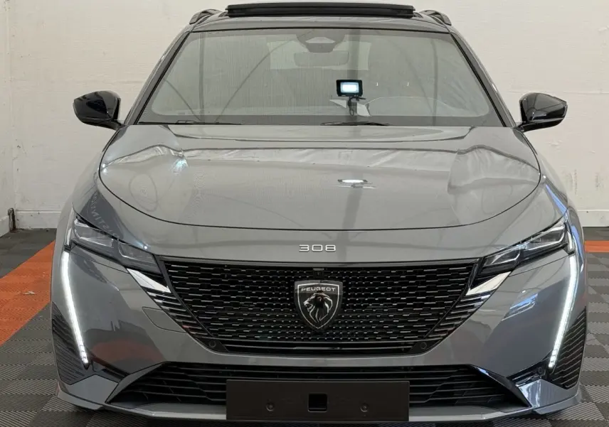 Vue frontale d'une Peugeot 308 Hybrid 136 e-DCS6 GT gris foncé avec calandre noire et feux LED verticaux allumés.