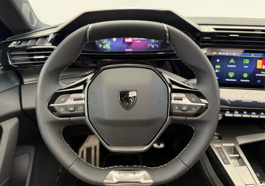 Volant cuir noir avec logo Peugeot et badge GT, vue frontale du poste de conduite de la 308 Hybrid 2024.