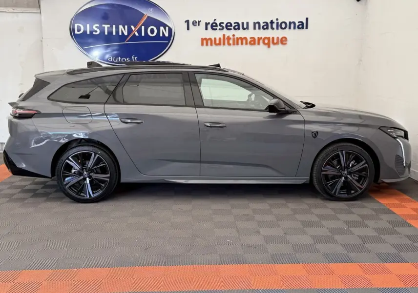 Profil droit d'une Peugeot 308 Hybrid 136 e-DCS6 GT gris foncé avec jantes noires et toit panoramique visible.