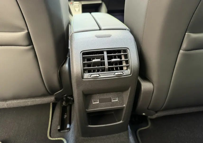 Vue rapprochée des aérateurs arrière et ports USB entre les sièges avant noirs d'une Peugeot 308 Hybrid 2024 gris foncé.