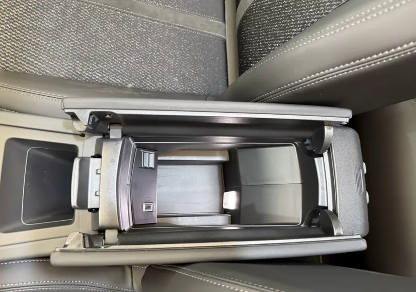 Vue plongeante sur le rangement central ouvert de la Peugeot 308 Hybrid 136 e-DCS6 GT avec sellerie gris foncé et coutures visibles.