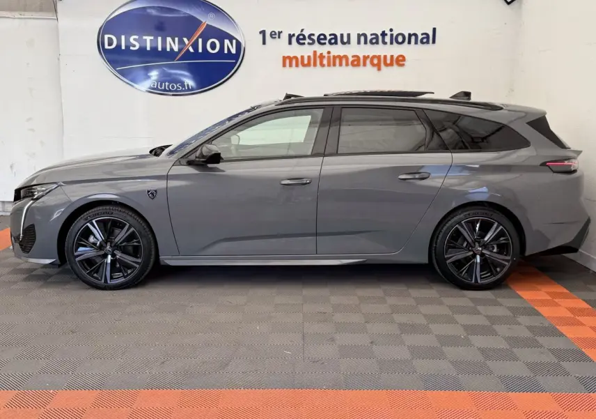 Profil droit d'une Peugeot 308 Hybrid 136 e-DCS6 GT gris foncé avec jantes noires et toit ouvrant en intérieur showroom.