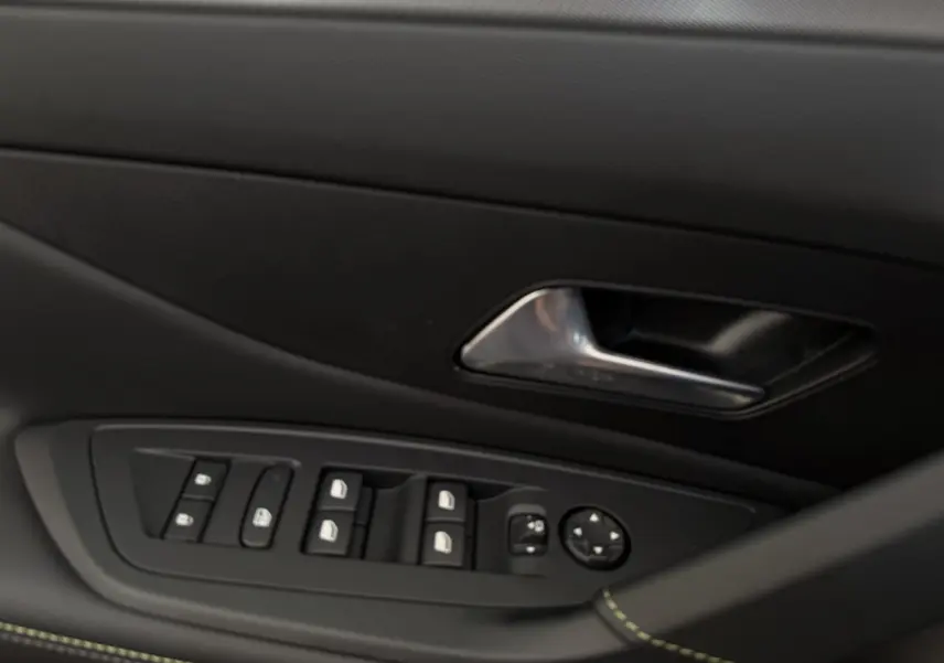 Gros plan sur la porte côté conducteur de la Peugeot 308 Hybrid gris foncé, avec commandes des vitres et poignée métal.