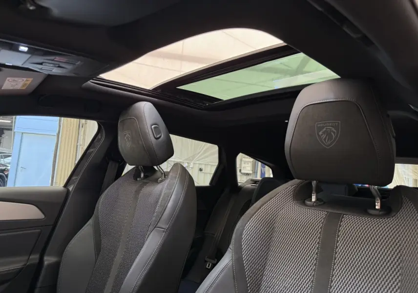 Vue intérieure rapprochée des sièges avant gris foncé avec logo Peugeot sur les appuie-têtes et toit ouvrant panoramique.