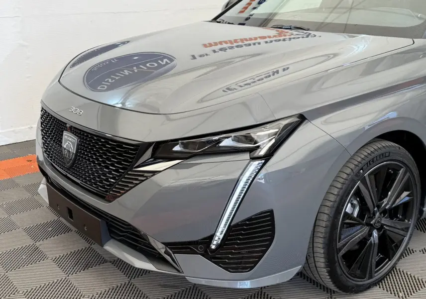 Vue 3/4 avant droit d'une Peugeot 308 Hybrid 136 e-DCS6 GT gris foncé avec phares LED et jantes noires.