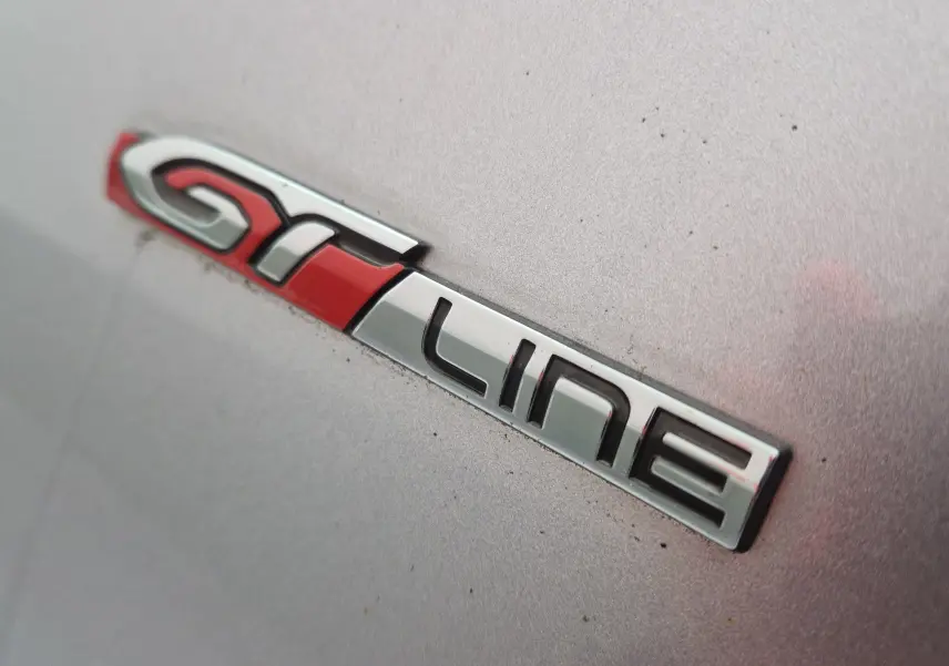 Gros plan sur l’inscription GT Line rouge et chrome sur la carrosserie gris Artense d’une Peugeot 308 SW.
