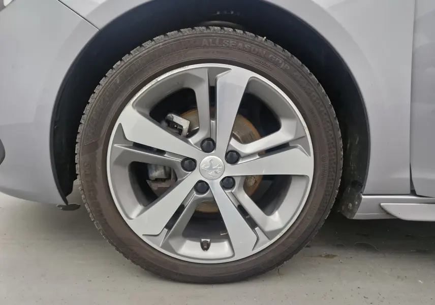 Gros plan sur la roue avant gauche d'une Peugeot 308 SW gris Artense, avec jante alliage 17 pouces et logo Peugeot central.
