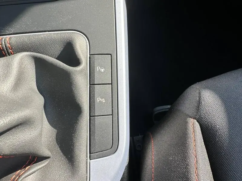 Gros plan sur la console centrale du SEAT Arona 2025, montrant le soufflet de levier de vitesses noir avec surpiqûres rouges et boutons de parking assisté.