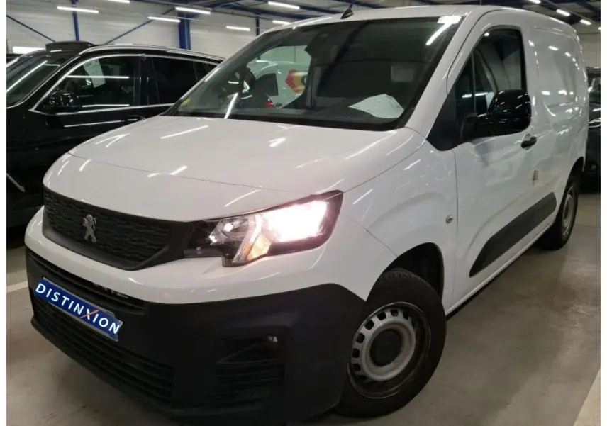 Vue 3/4 avant droit du Peugeot Partner Fourgon blanc 2022 avec phares allumés et pare-chocs noir mat distinctif.