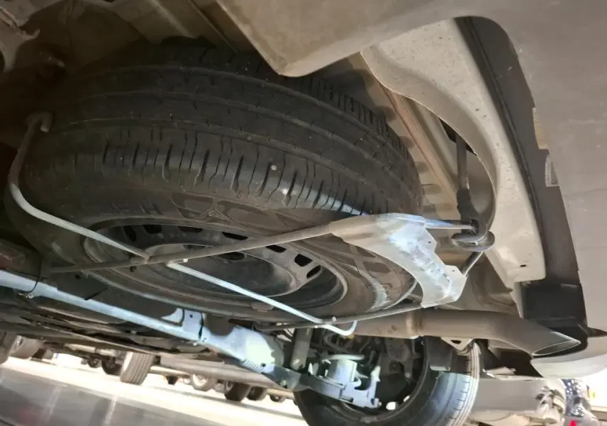 Vue en contre-plongée sous le Peugeot Partner Fourgon blanc, montrant la roue de secours fixée sous le châssis arrière.