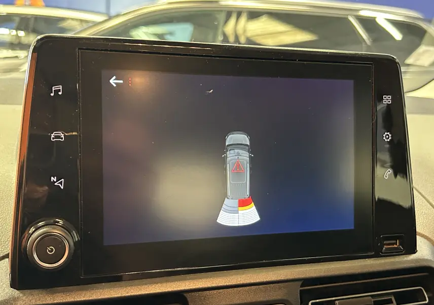 Écran tactile du GPS montrant l'alerte de proximité arrière du Peugeot Rifter gris sable, version BlueHDi 2019.