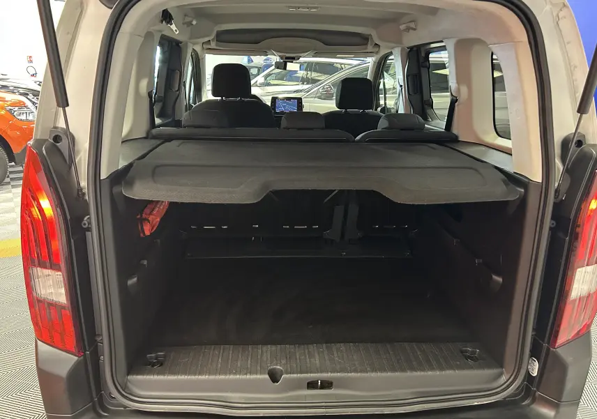 Coffre ouvert vu de l'arrière d'un Peugeot Rifter gris sable 2019 avec cache-bagages et sièges arrière visibles.