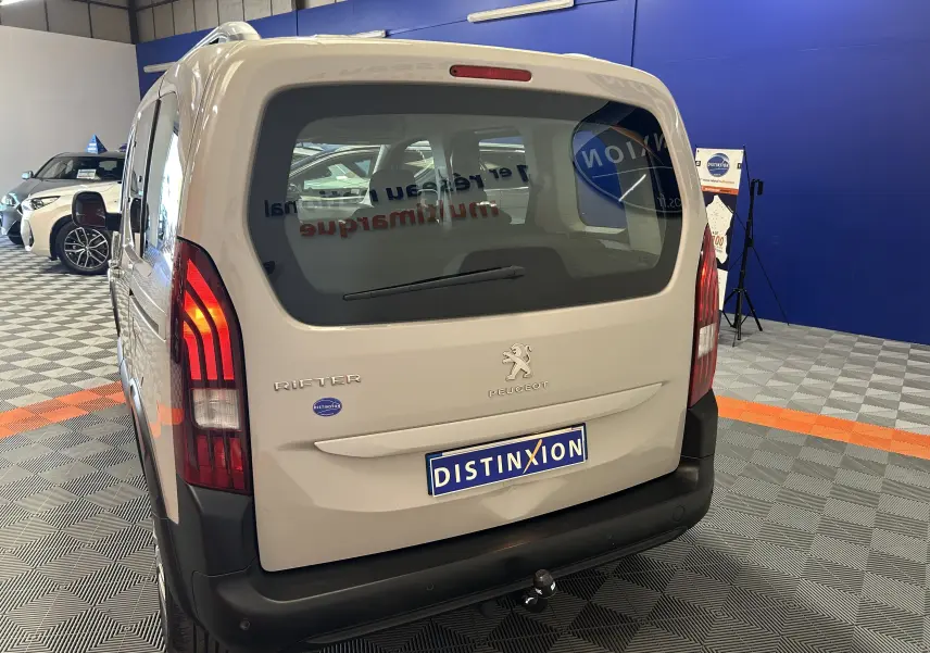 Vue arrière d'un Peugeot Rifter gris sable 2019 avec attelage visible dans un showroom.
