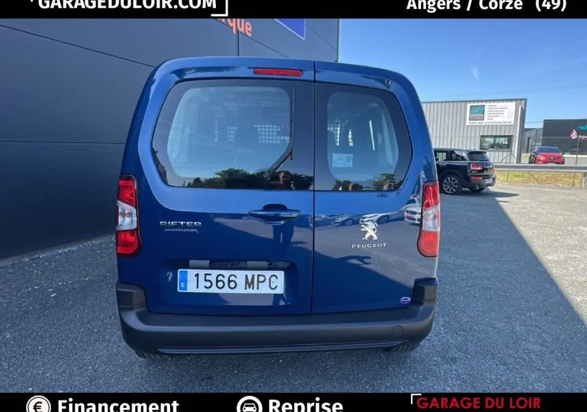 Vue arrière d'un Peugeot Rifter bleu 2024 avec portes battantes et logo visible sur un parking extérieur.