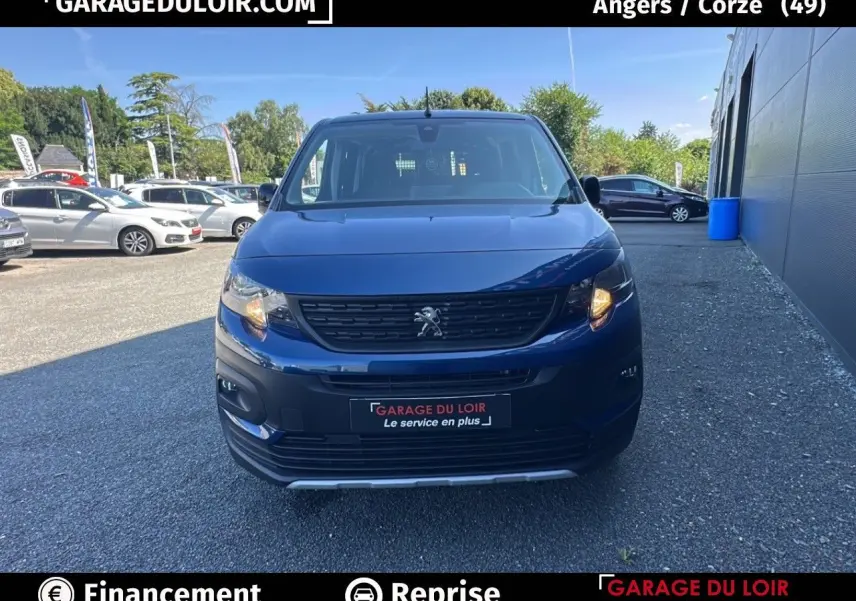 Vue avant d'un Peugeot Rifter bleu 2024 avec calandre noire et feux allumés sur parking extérieur.