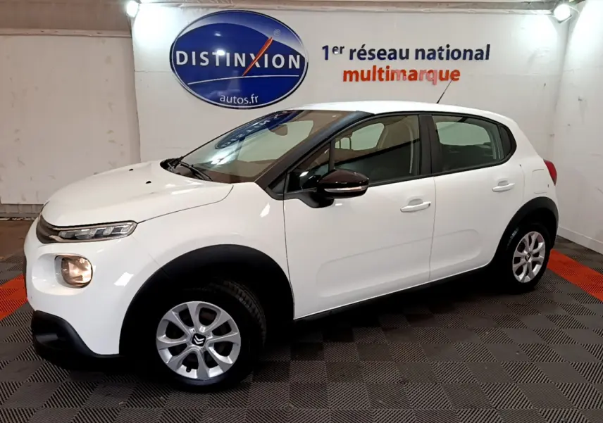 Citroën C3 blanche vue de profil côté gauche, avec feux avant allumés dans un showroom.