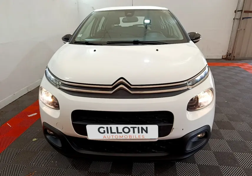 Vue frontale d'une Citroën C3 blanche de 2019 avec phares allumés dans un garage intérieur.