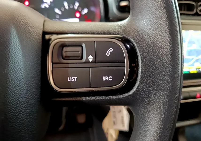 Gros plan sur les commandes gauche du volant noir de la Citroën C3 PureTech 2019 avec écran tactile en arrière-plan.