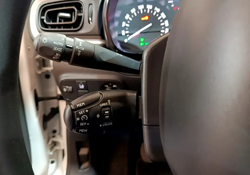Gros plan sur les commandes du régulateur de vitesse et des phares côté gauche du volant d'une Citroën C3 blanche de 2019.