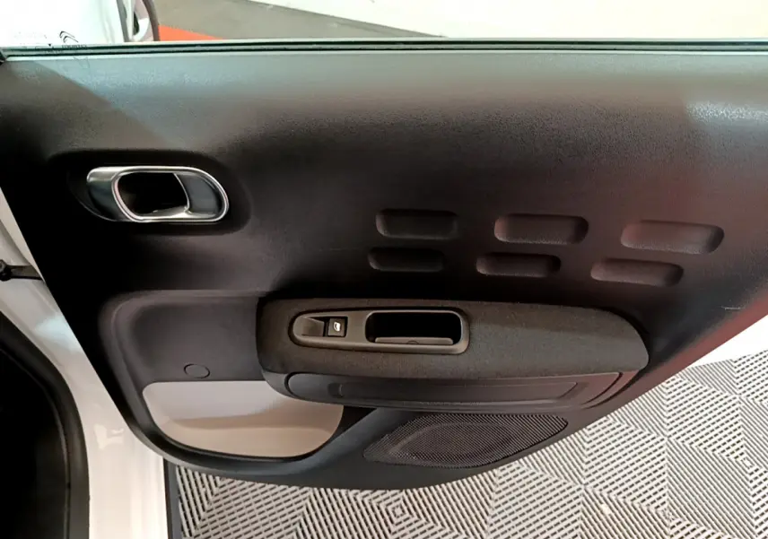 Vue intérieure de la porte côté gauche d'une Citroën C3 blanche, avec poignée et commande de fenêtre noire.